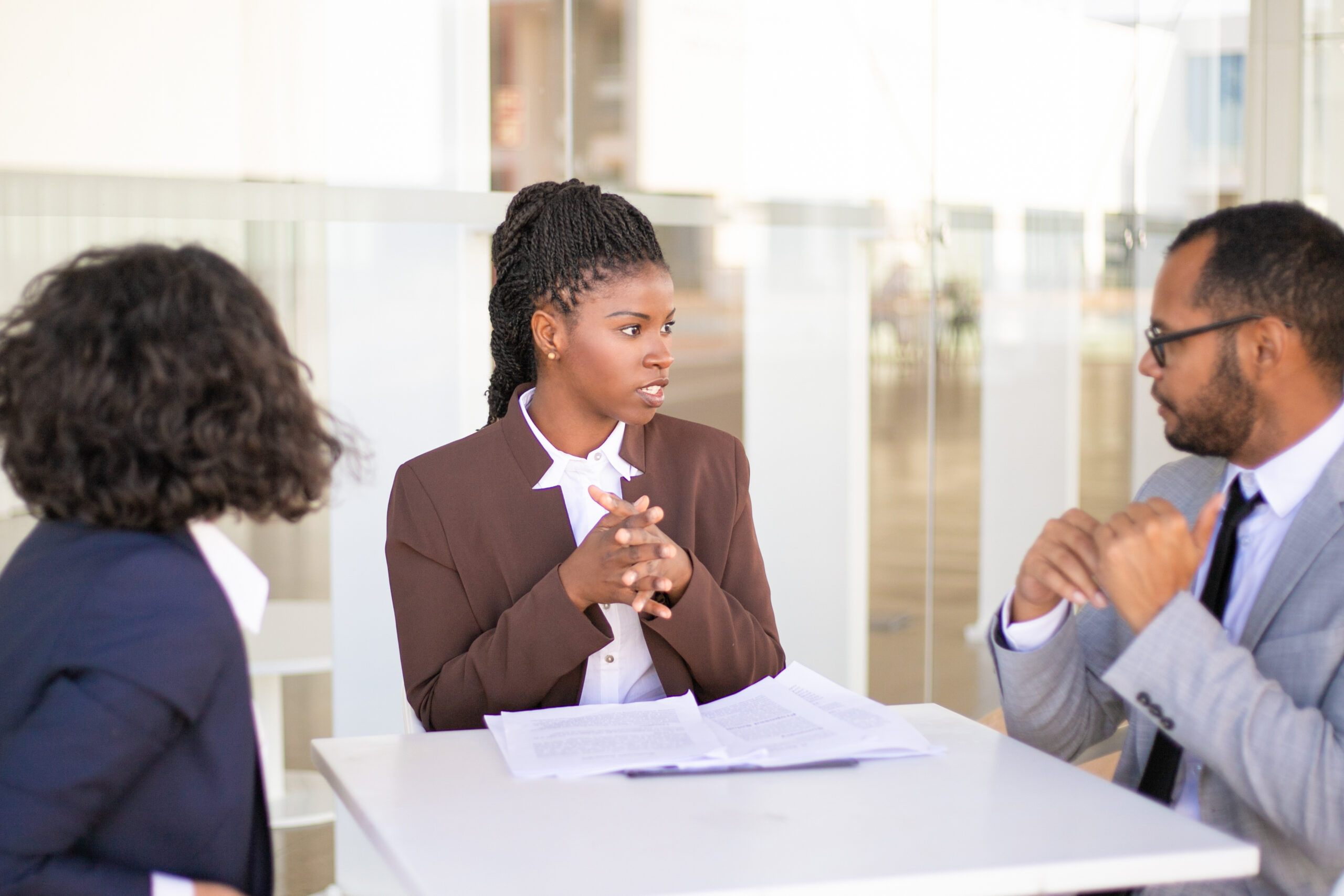 Advisor explaining document details to customers. Multiethnic business man and women sitting at table outdoors and talking. Paperwork or expertise concept