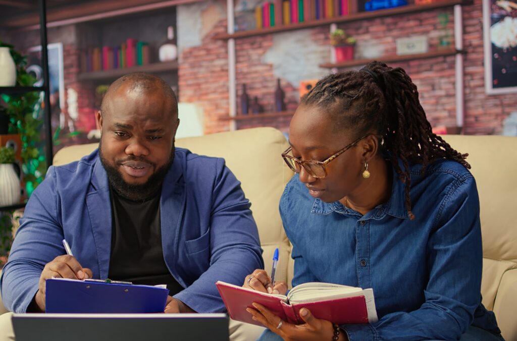 Black man and woman writing a report with information from notebook and archived files, improving networking skills and achieving career independence. Freelancers solving tasks. Camera A.